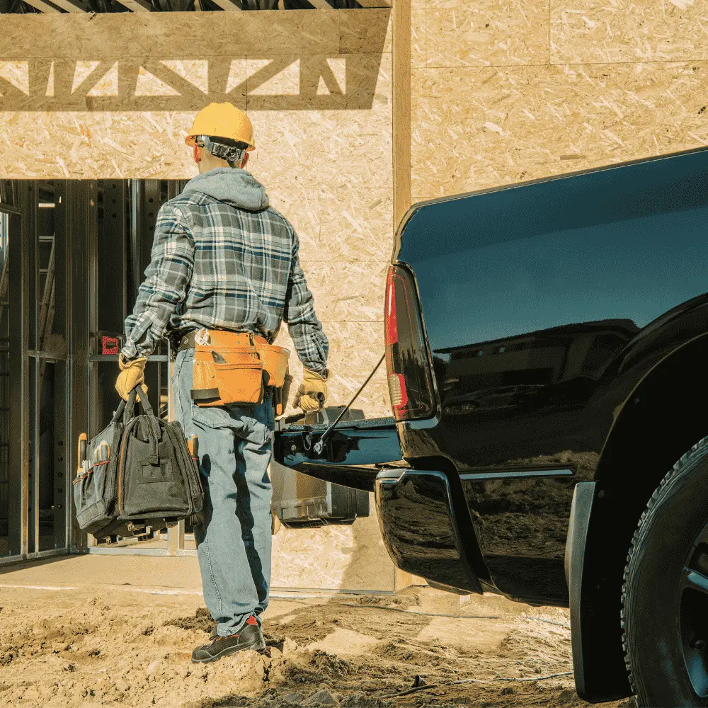 construction worker carrying a tool bag and walking from a black pickup truck toward a building under construction