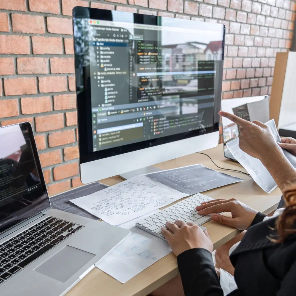 people collaborating on website code displayed on desktop and laptop screens