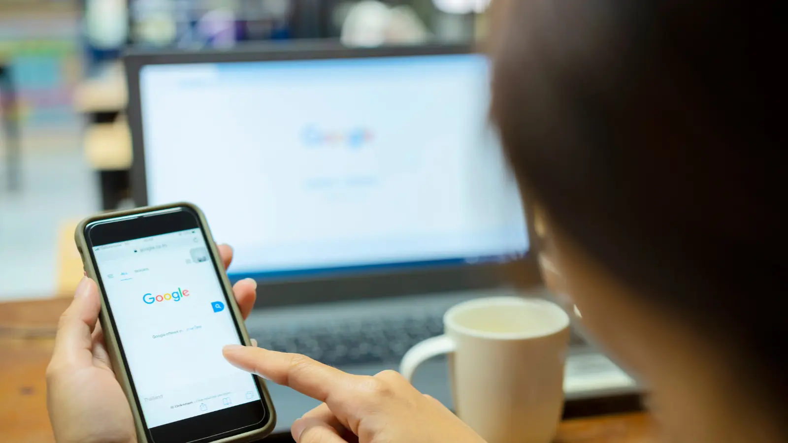 person using google search on a smartphone with a laptop in the background