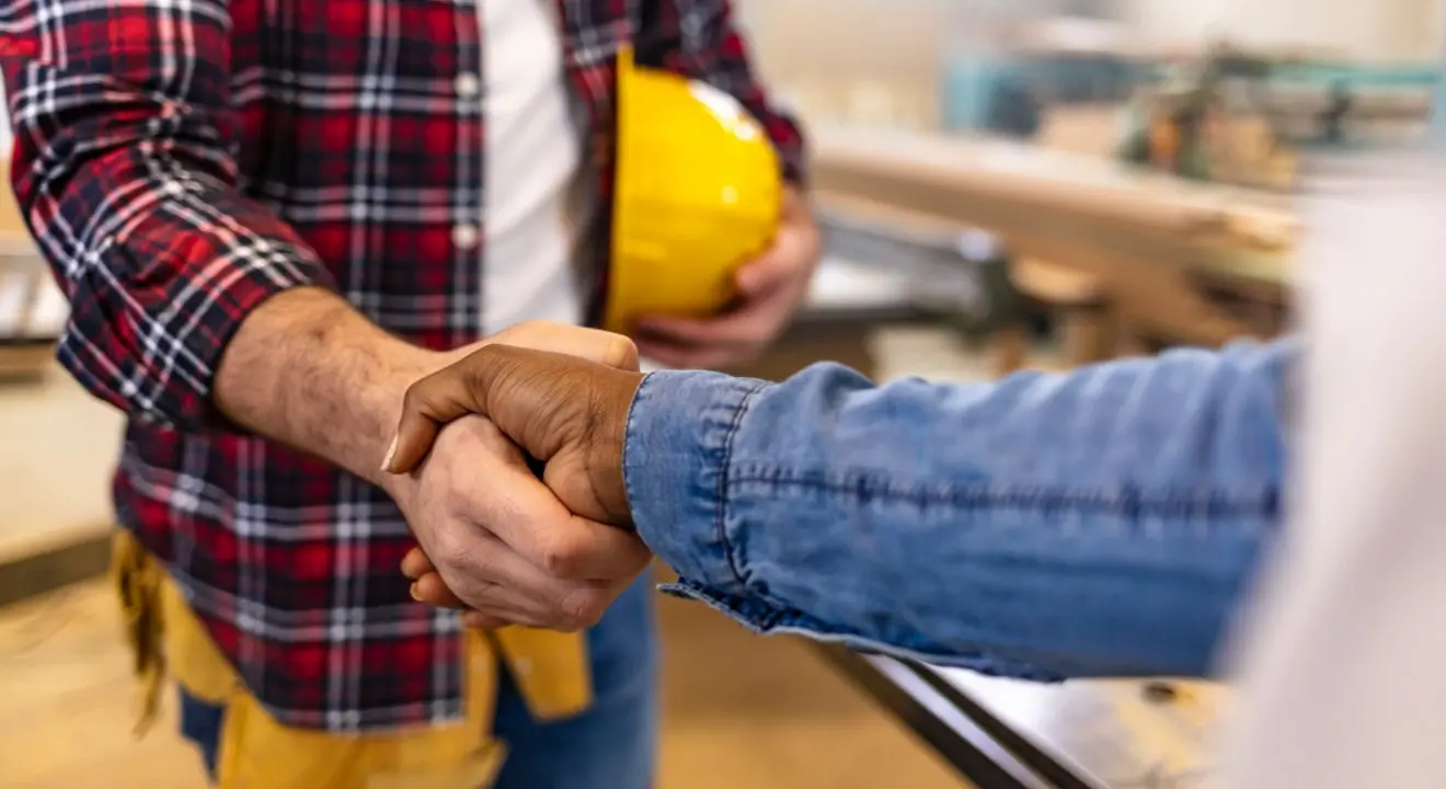 two people shaking hands, one holding a yellow construction helmet